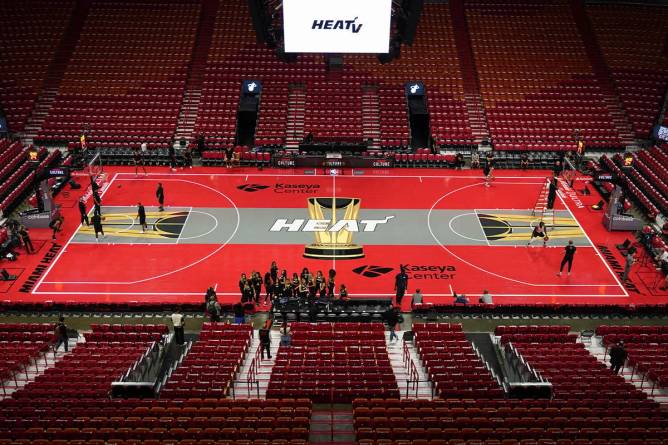 Miami Heat court, red floor with grey stripe in the middle. The NBA in-season tournament trophy and “heat” logo in center of court. The stadium is mostly empty with teams warming up.