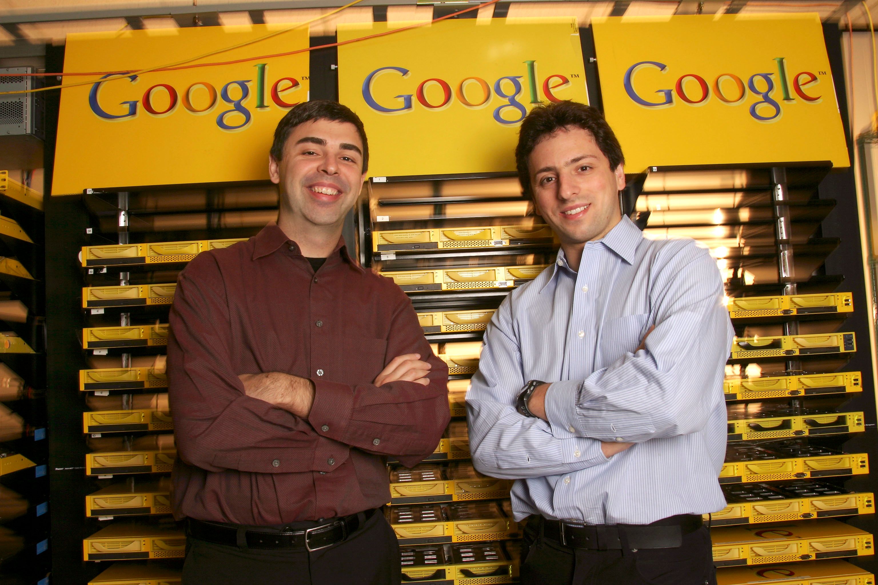 Two men in button up collared shirts standing in front of a gridded wall of yellow trays.