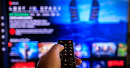 A man holding a TV remote pointing it at his TV surfing a streaming platform for something to watch