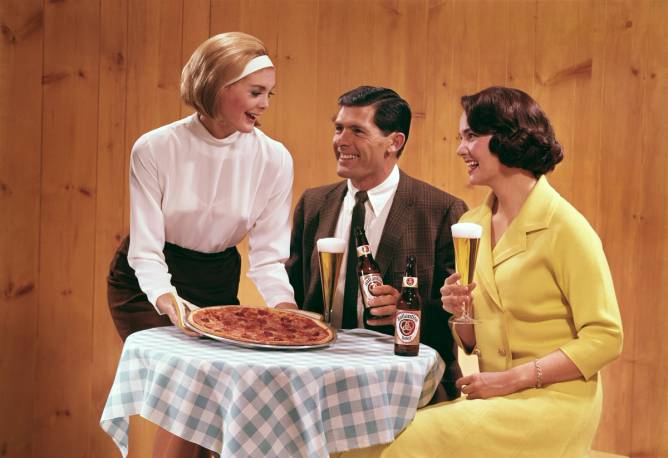 a women serving pizza and beer to two people