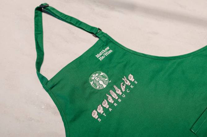 A close up image of a green Starbucks apron, with Starbucks spelled out in American sign language