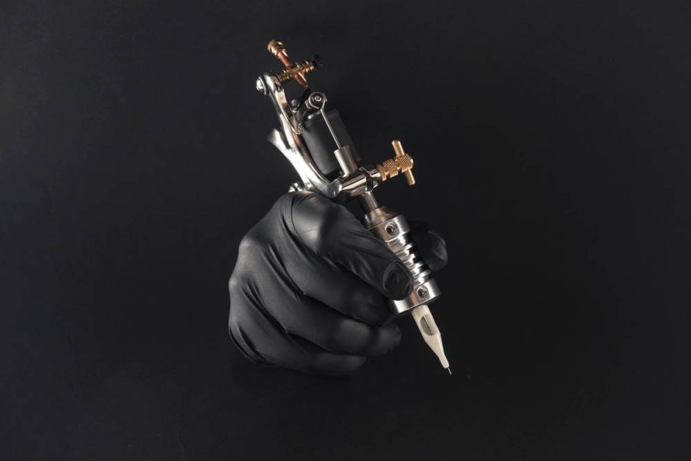A gloved hand holds a tattoo machine.