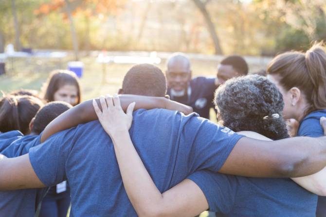 A group of people in matching T-shirts put their arms around each other and huddle.