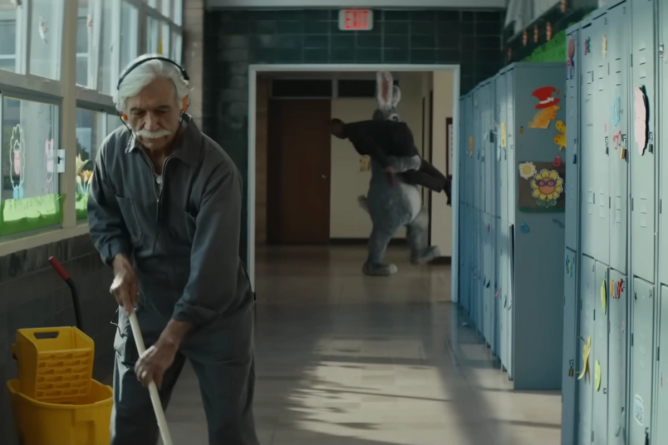 a janitor mopping in a school with a person wearing a rabbit costume in the background carrying a person, in a still from a Tubi commercial