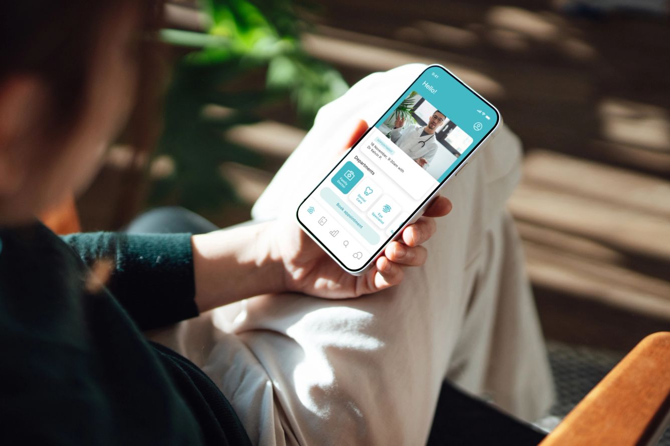 Over the shoulder view of young woman holding smartphone, having a telemedicine consultation with doctor.