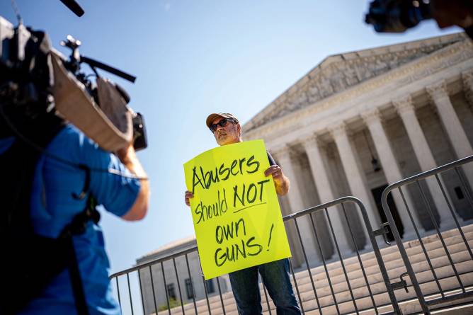 A protester with a sign that says "abusers should not have guns" outside the Supreme Court