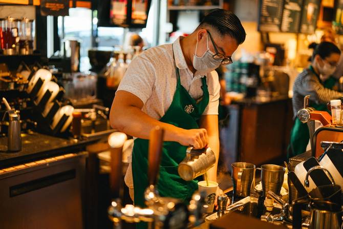 a photo of a Starbucks employee wearing a mask while making a coffee