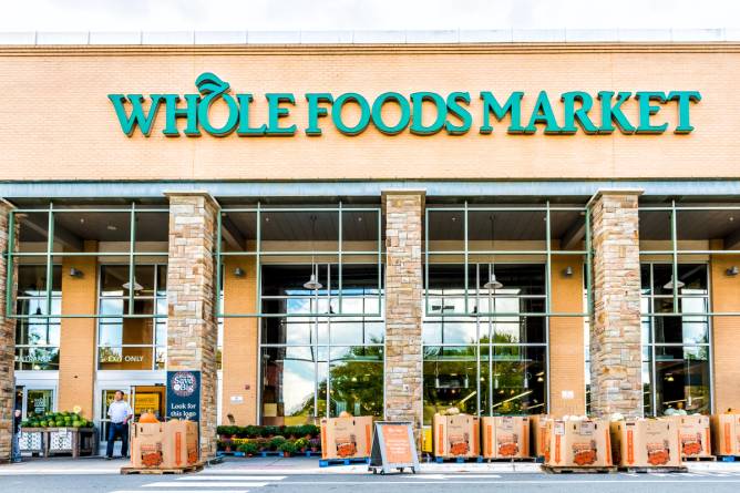 Green Whole Foods Market grocery store sign on exterior building in city in Virginia with people walking and autumn displays of pumpkins for Halloween