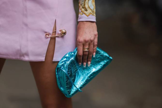 A gold safety pin is pinned to the slit in a pink Versace skirt worn by  model. n 