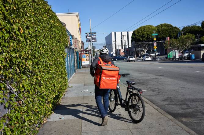A DoorDash delivery worker walks their bike down a street.