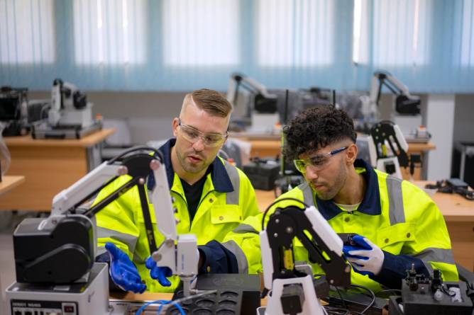 Technicians in a classroom working with a robotic arm.