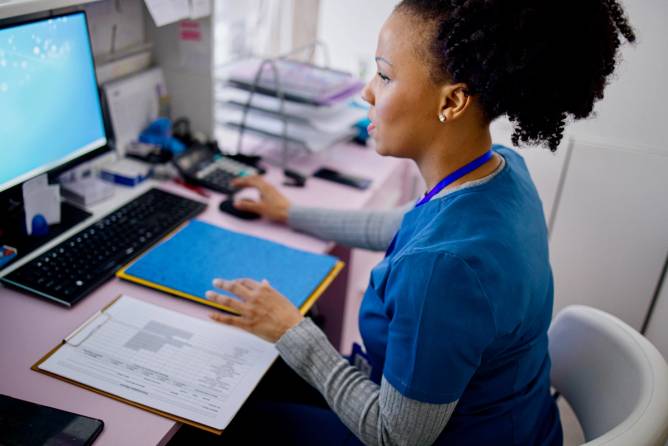 Black woman using computer to work as nurse in the private clinic.