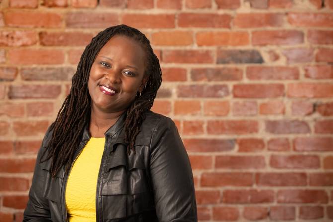 A picture of Demetris Cheatham in wearing a yellow shirt and leather jacket, standing in front of a brick wall