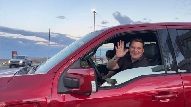 Jim Farley waves from the cab of an F-150 Lightning.