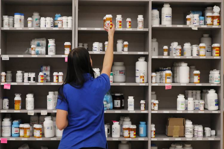 A pharmacy technician grabs a bottle of medicine off a shelf at a pharmacy