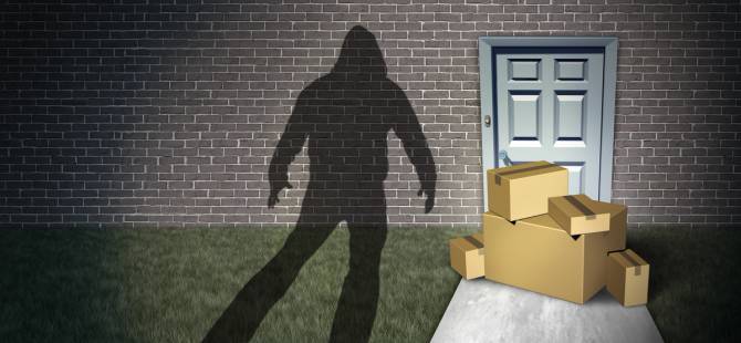 A shadow of a hooded figure near packages outside a residence's front door. 