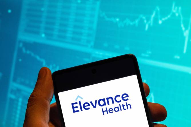 A photo illustration of a person holding a phone with "Elevance Health" written on the screen.