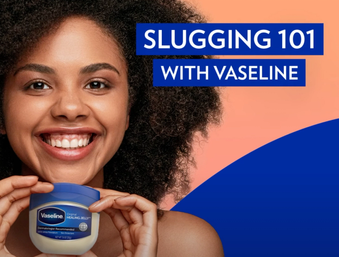 In a still from a Vaseline video on YouTube a smiling woman holds a jar of Vaseline under text, "Slugging 101 with Vaseline." 