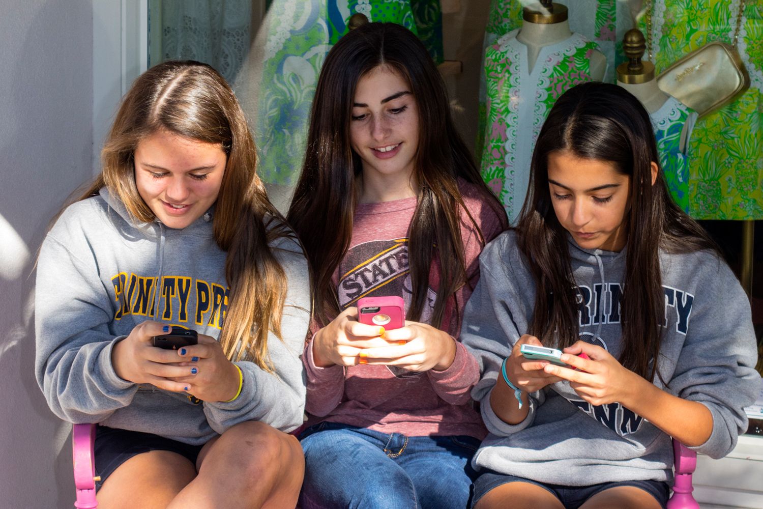 Three teenage girls sitting on a bench and texting on their smartphones.