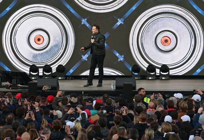 Image of Elon Musk on stage presenting about batteries, with image of batteries behind him