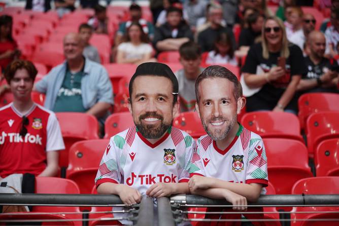 A Wrexham fan with novelty masks showing Wrexham Owners Rob McElhenney (L), and Ryan Reynolds (