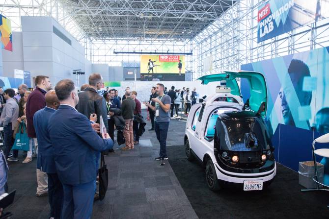 People at a conference listening to a man in front of a futuristic vehicle