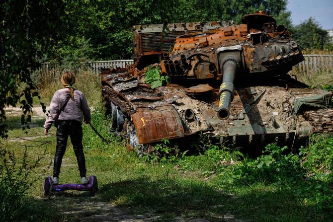 A teenager rides a hoverboard past a destroyed Russian army tank in the village of Lukashivka, Chernihiv region