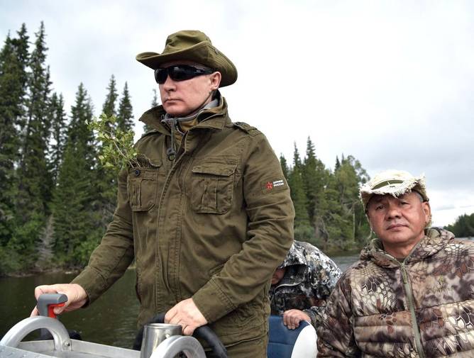 Russian President Vladimir Putin (L), accompanied by defence minister Sergei Shoigu, guides a boat during his vacation in the remote Tuva region in southern Siberia