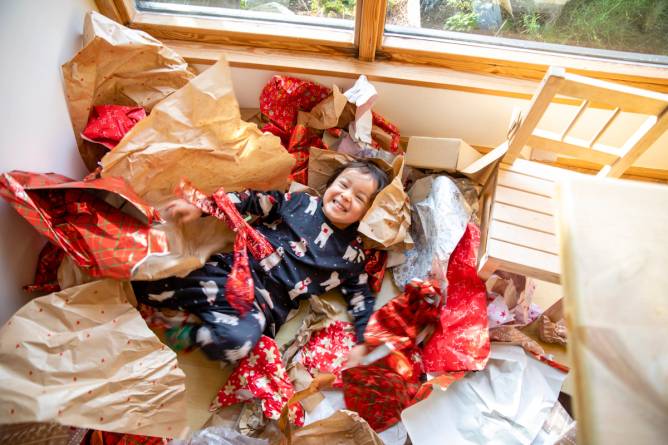 A toddler laughs while playing in a pile of wrapping paper. 