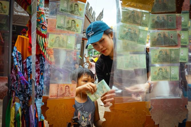 A mother and child slide a 20 baht offering into a plastic sleeve.