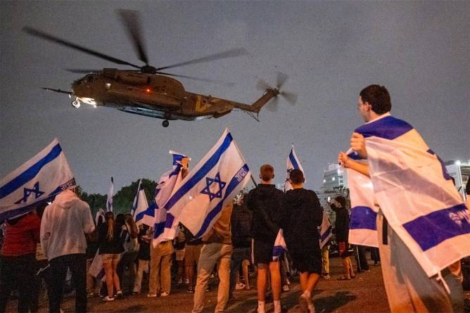 People wave flags and cheer as a second helicopter with Israeli hostages released earlier by Hamas lands.