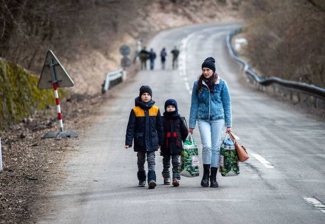 A woman with two children and carrying bags walk on a street to leave Ukraine after crossing the Slovak-Ukrainian border in Ubla, eastern Slovakia