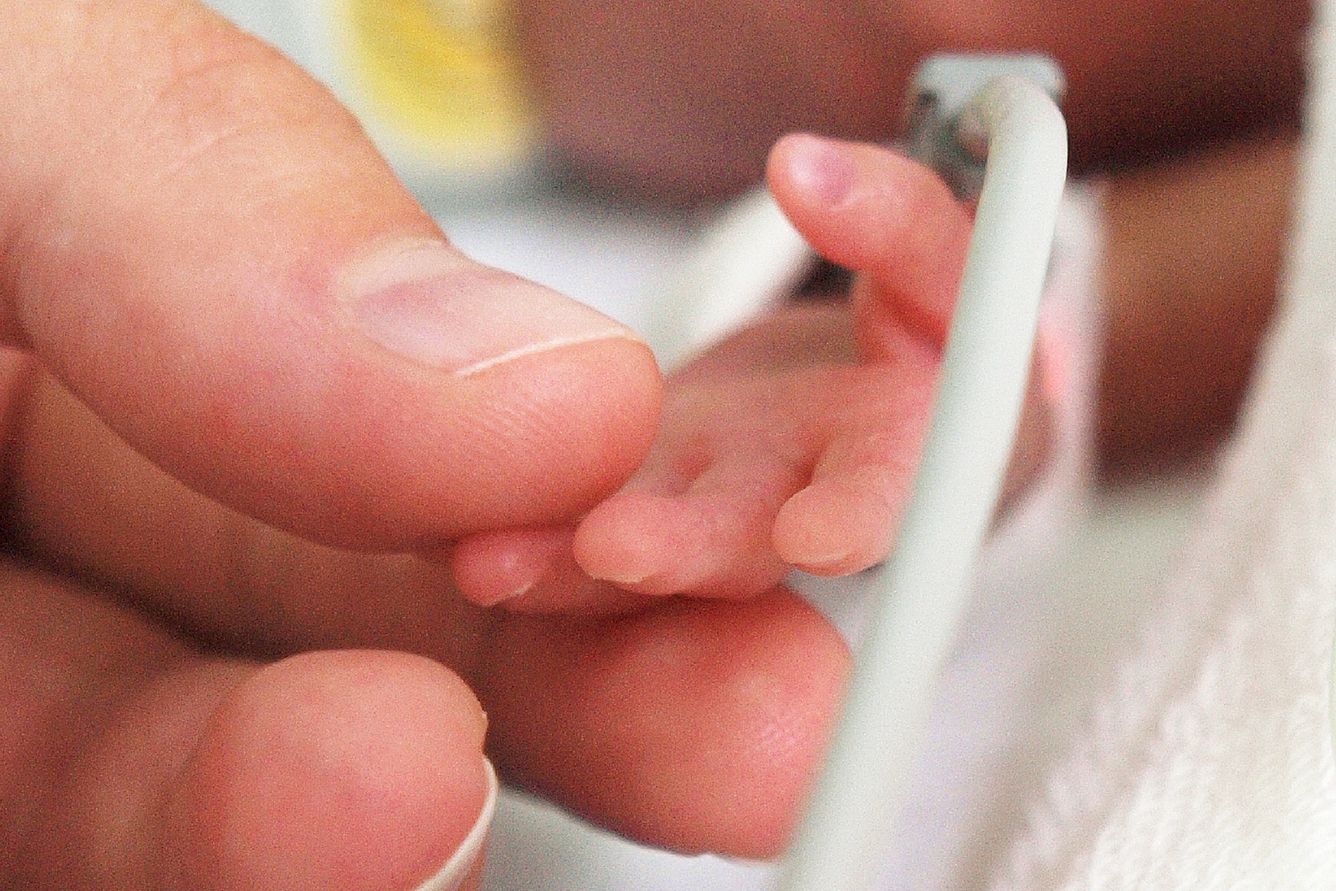 Mother is holding a tiny hand of her preterm baby in the NICU.