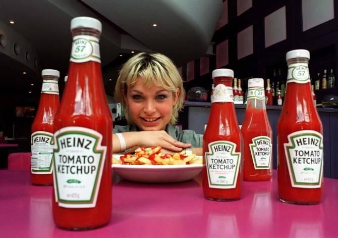 A woman poses with a plate for french fries with five bottles of Heinz ketchup in the foreground. 