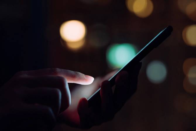 a woman's hand near a phone on a dark background