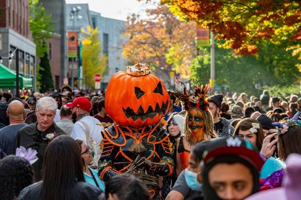 A large pumpkin-headed costumed reveller walks with others through a crowded street on Halloween in Salem, Massachusetts on October 31, 2021