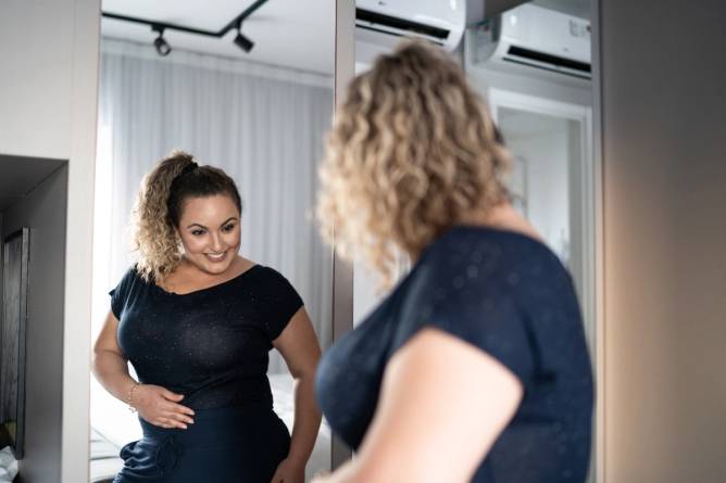 Woman getting dressed in front of a mirror at home.