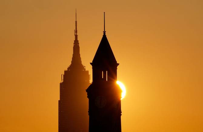 The sun rises behind the Empire State Building in New York City and the Lackwanna clock tower in Hoboken, New Jersey