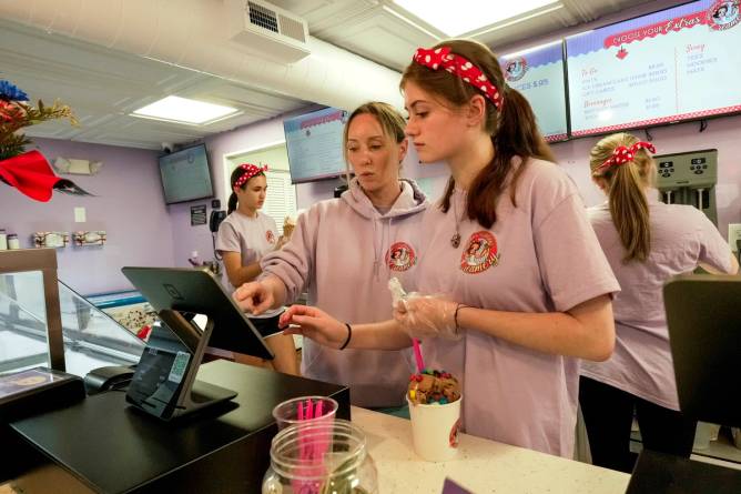 Two teenage girls work the cash register at an ice cream shop.
