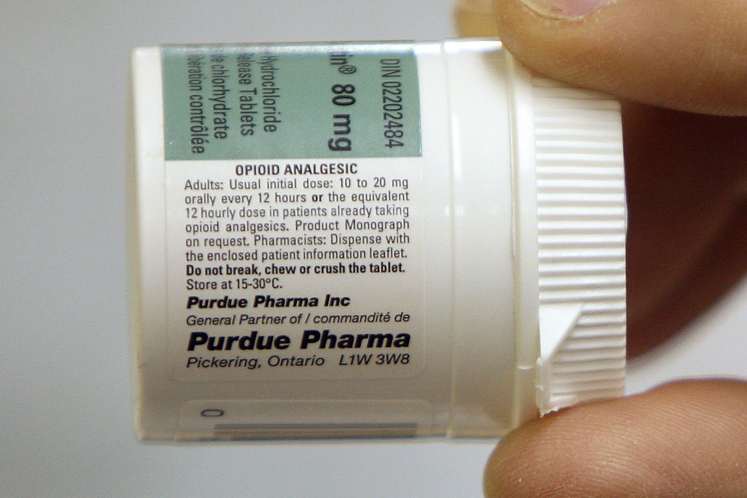A close range shot of a hand holding a pill bottle labeled with Purdue Pharma and dosage information.