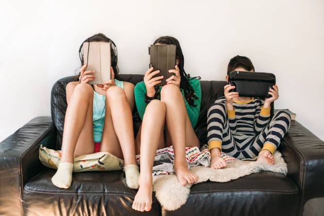 Three kids with electronic devices on a sofa.