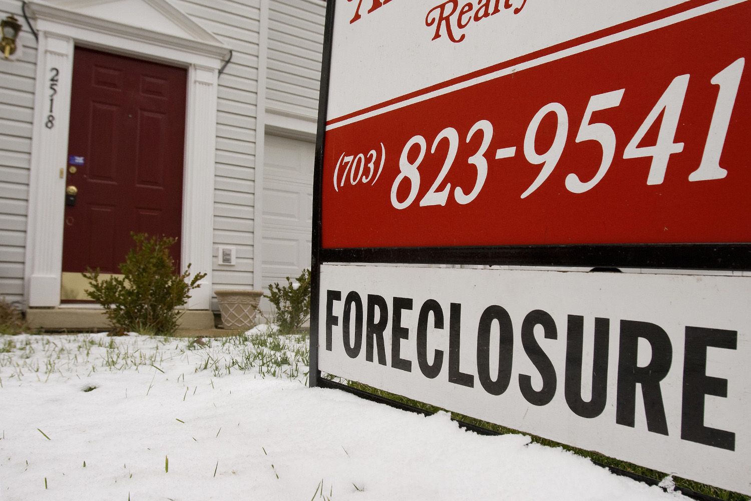 Foreclosure sign sits in snow in front of house.