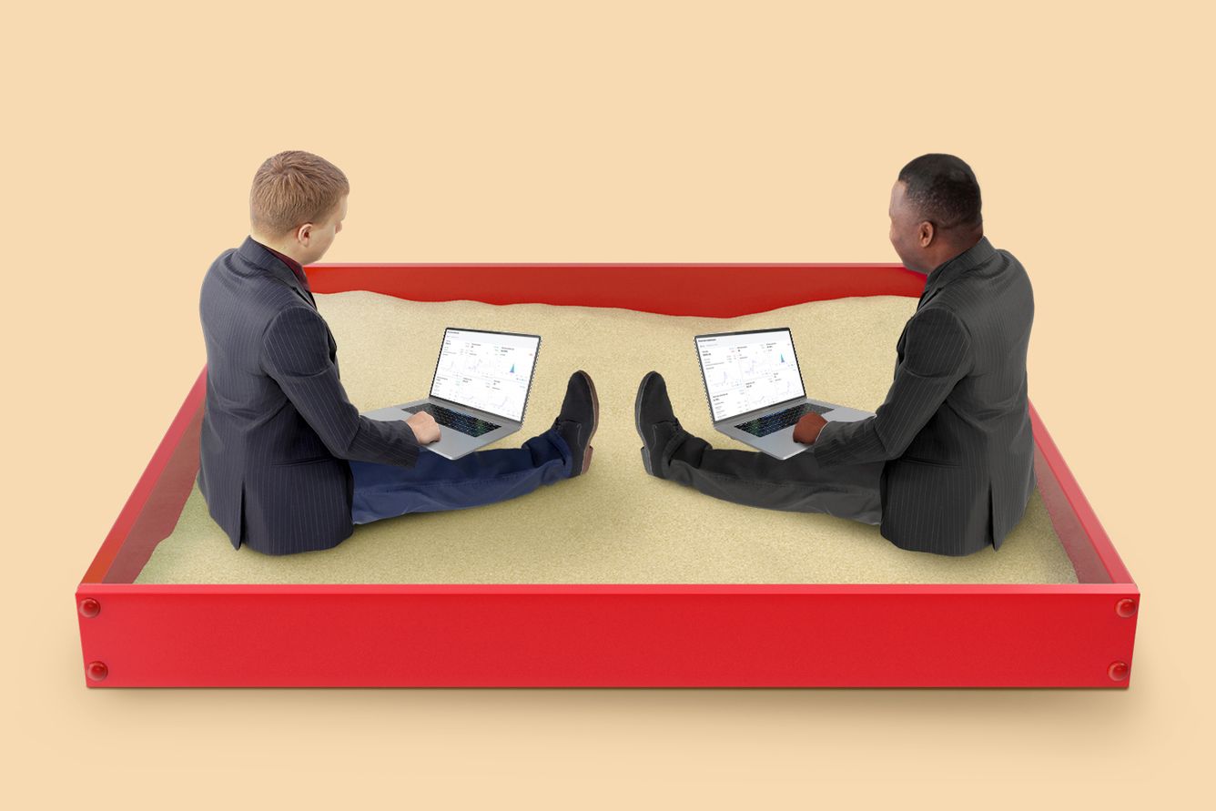 two suit and tie types on their laptops in the sand