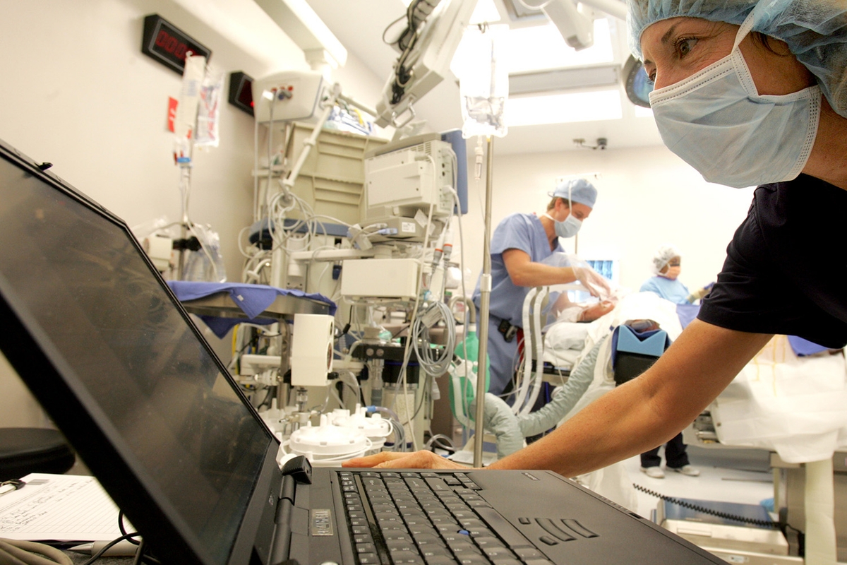 A nurse in a face covering looks intently at data on an open laptop screen.
