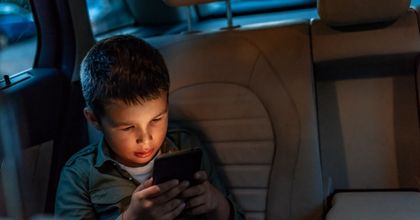 A male child playing on a smartphone in the back of a car