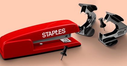 A red stapler with the Staples logo embossed on the side next to a couple of staple removers