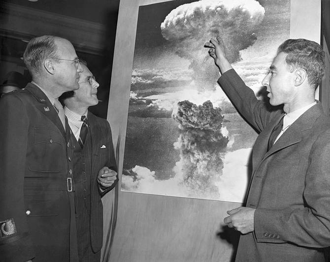 American physicist Dr. Robert Oppenheimer (1904 - 1967), points to a picture of the atomic bomb explosion over Nagasaki, Japan, as scientist Henry D. Smyth (1898 - 1986) (second left), major General Kenneth D. Nichols (1907 - 2000) (second right), and scientist Glenn Seaborg (1912 - 1999) look on, 1940s. 