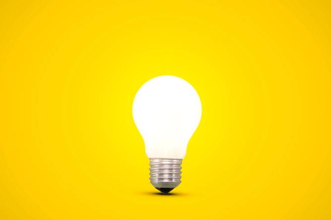 Image of a glowing lightbulb on a bright yellow background.