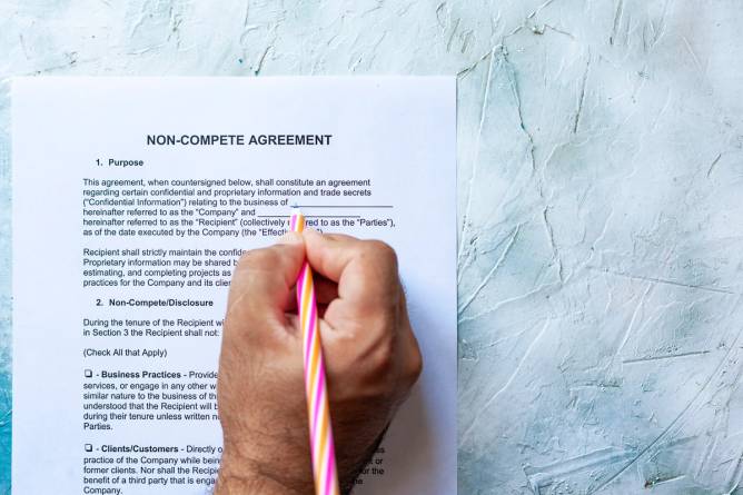 Close-up of a hand filling out a noncompete form. 