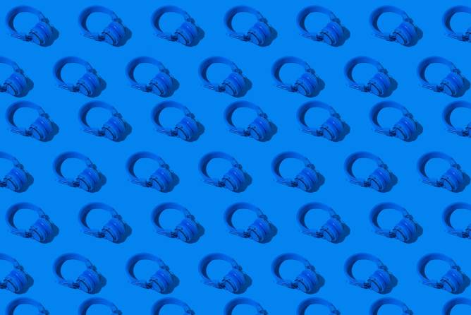 a pattern of blue wireless headphones with a hard shadow on a blue background